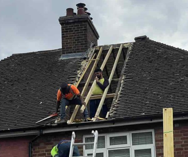 This is a photo of a roof repair being carried out. A section of the roof has been stripped and two roofers are replacing the rafters. Works being carried out by CNB Roofing Pontefract